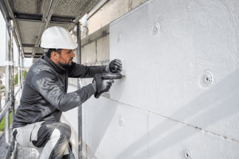 Artisan posant et chevillant des panneaux isolants sur une façade en ITE